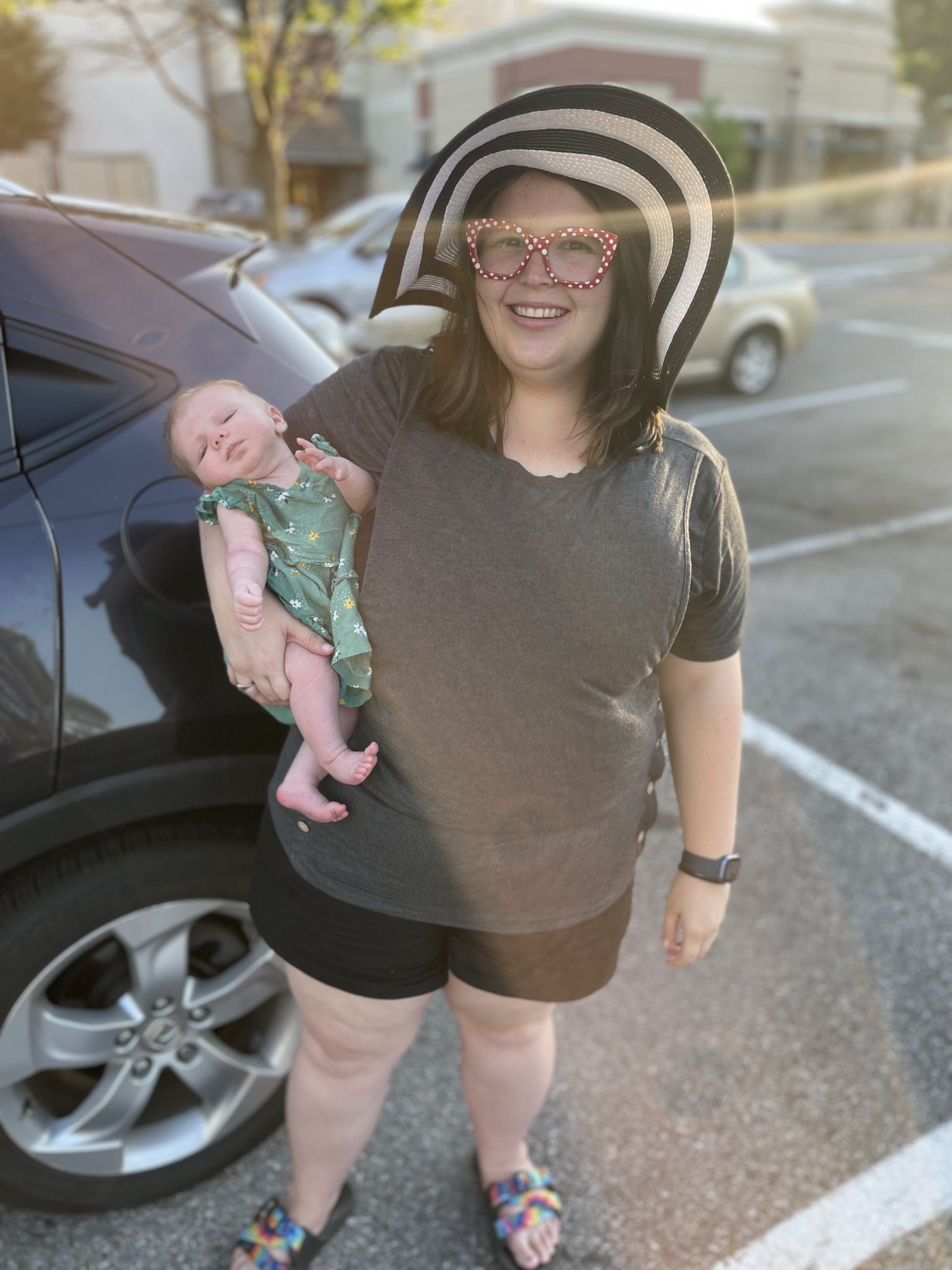 Me holding my baby daughter Shara while wearing a black and white floppy hat, gray shirt, and black shorts.